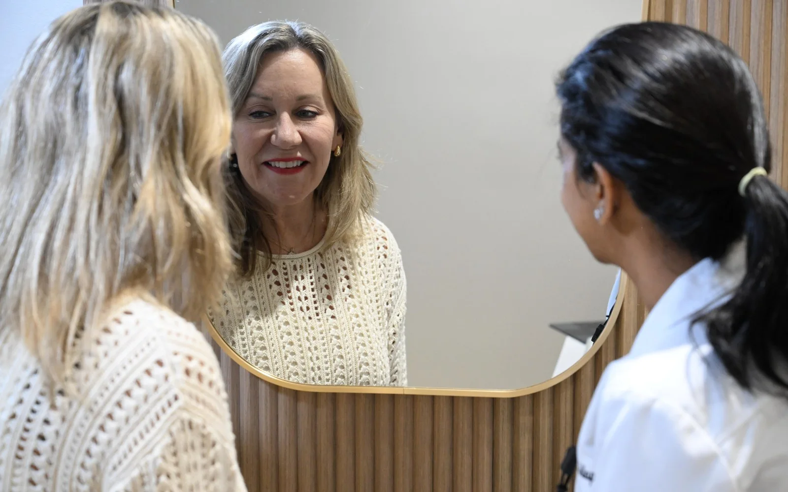 Patient smiling at her new full-arch smile in the mirror while Dr. Meenachi Sellappan watches — Smile Spot Dentistry, Venice FL